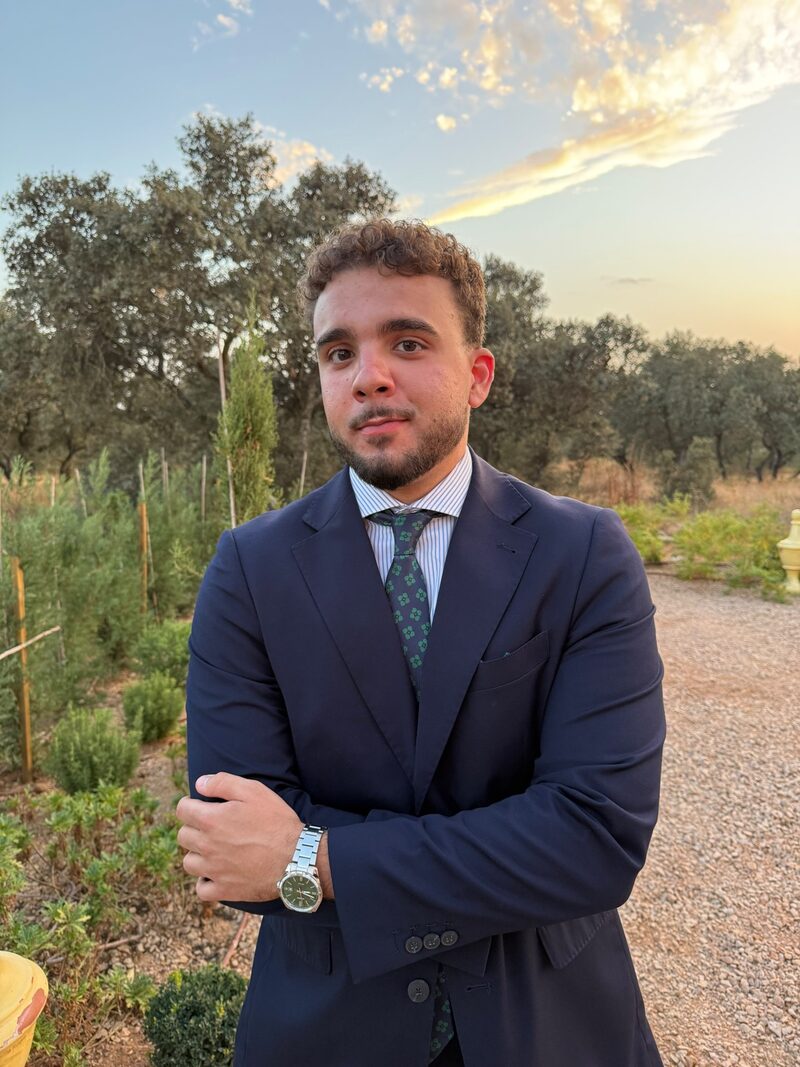 Carlos Martínez Parra, graduado en ADE y Economía, con traje azul marino en un entorno de dehesa extremeña